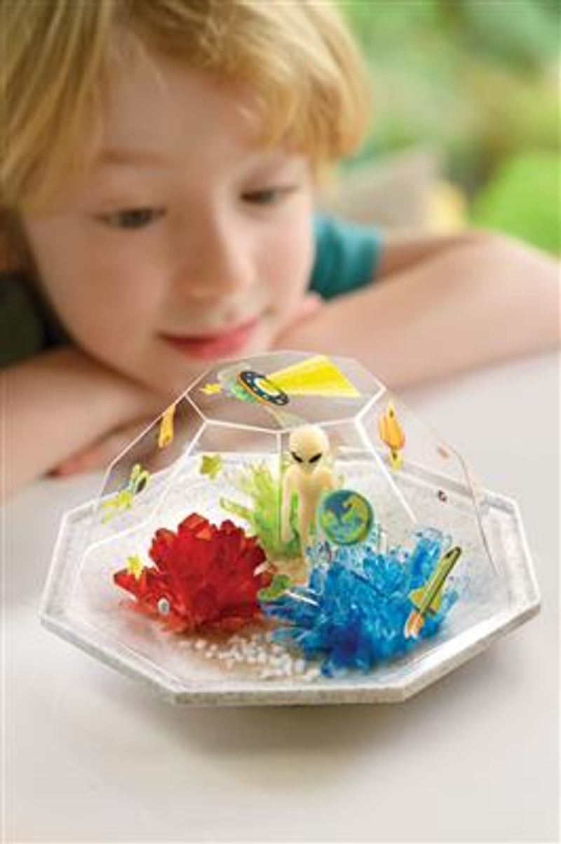Kind bekijkt een ruimteterrarium met rode en blauwe kristallen, een alien en ruimtestickers.