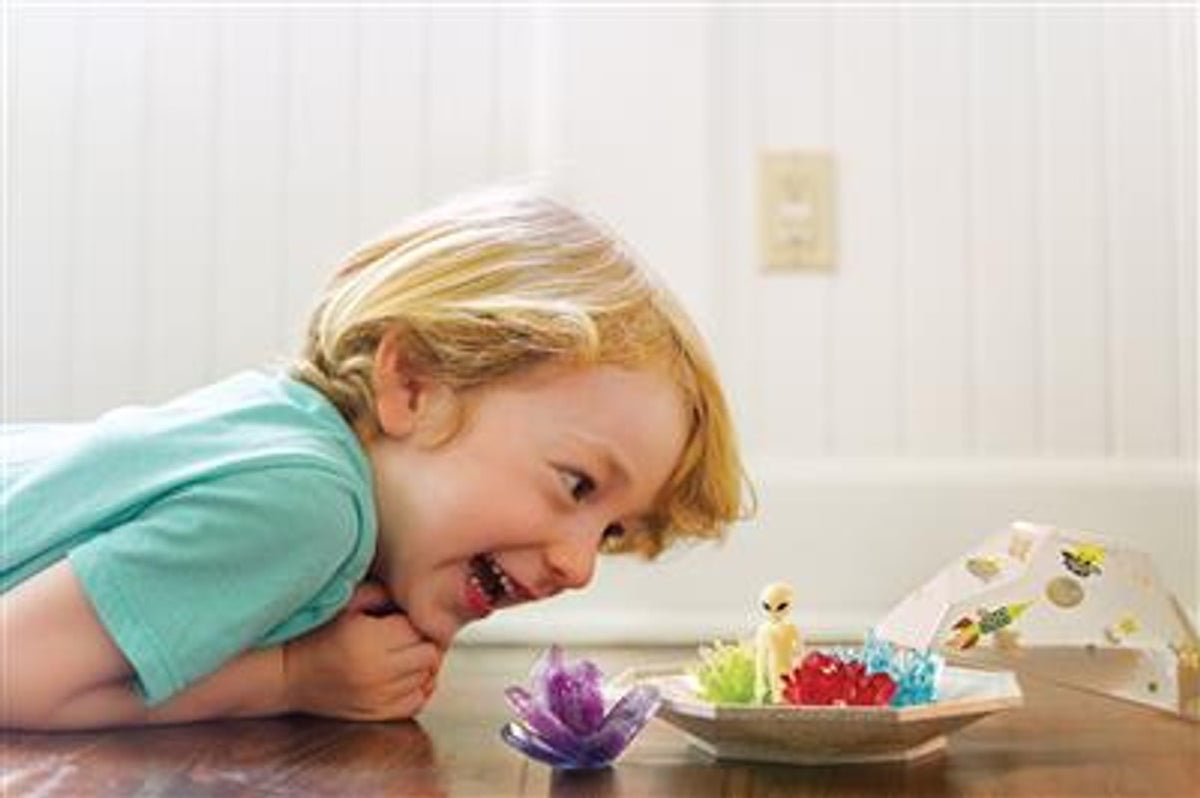 Kind kijkt naar gekleurde ruimtekristallen en een alien op tafel, met de terrariumkap ernaast.