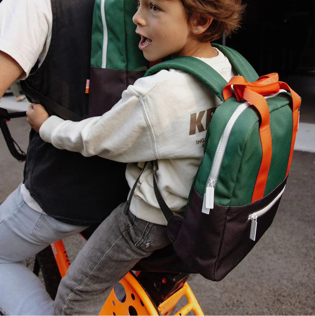 Kind achter op een fiets met de Hello Hossy Mini Dark Green rugzak, met oranje handgrepen en een donkere voorzak.
