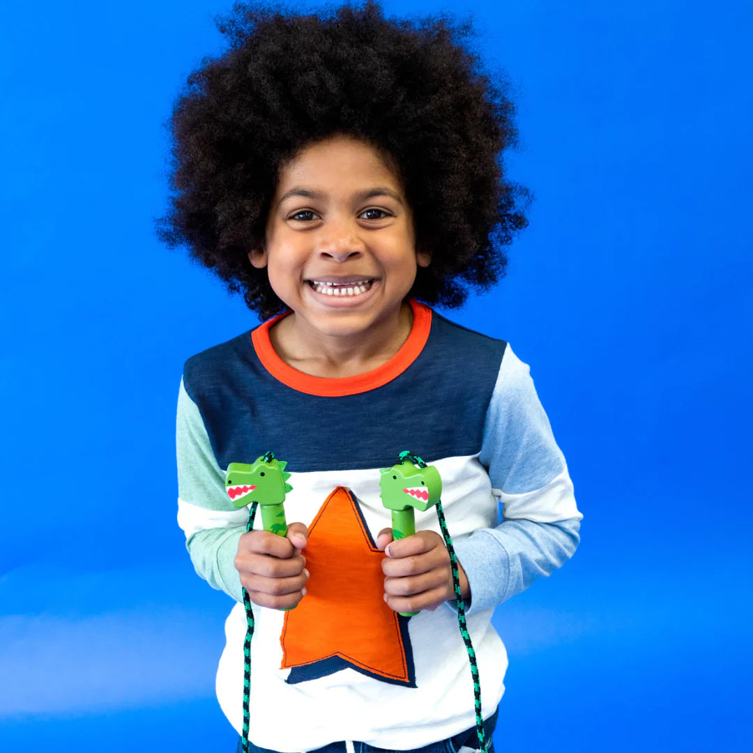 Kind houdt een dino-springtouw met groene dinosaurushandgrepen vast tegen een blauwe achtergrond.