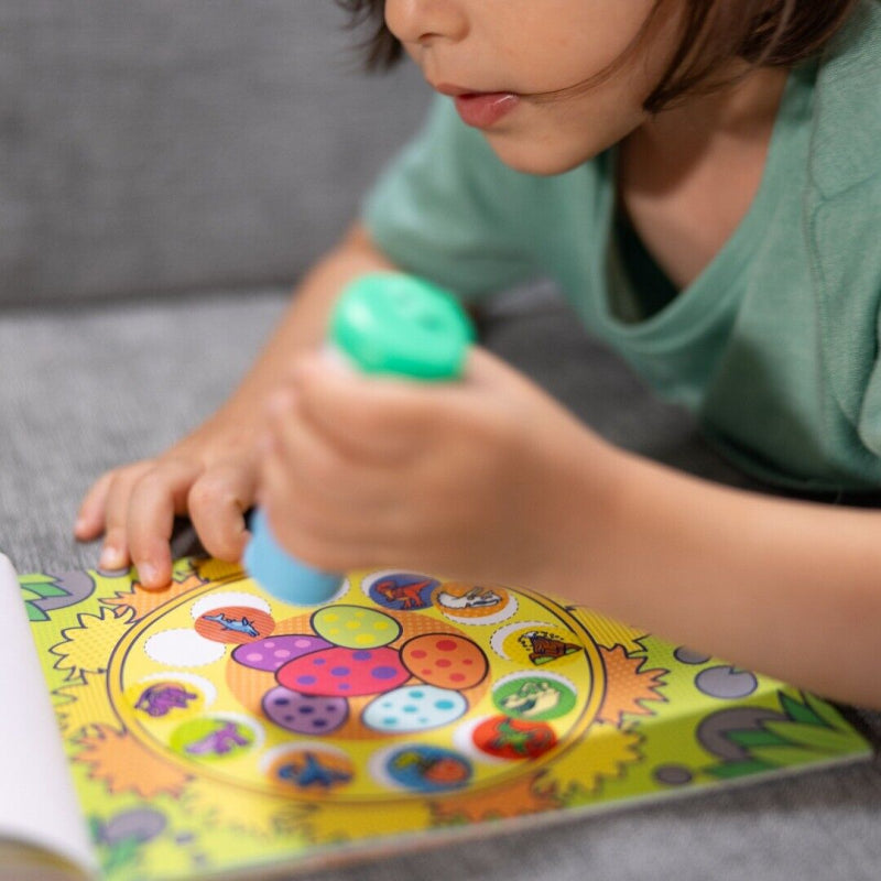 Kind gebruikt de groene dinosaurus-stickerstempel van Sticker Wow op een kleurrijke pagina uit het activiteitenboek.