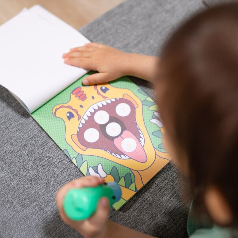 Kind houdt de groene dinosaurus-stickerstempel boven een activiteitenpagina met een grote dinosaurusbek.