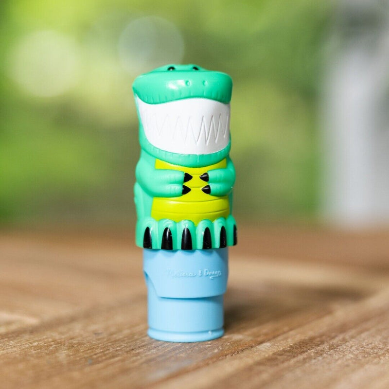 Groene dinosaurus-stickerstempel met witte tanden, gele buik en blauwe basis op een houten tafel.