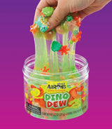 Een hand rekt felgroen Crazy Aaron's Dino Dew slijm met dinosaurus-bedeltjes en kralen uit een open pot.