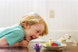 Kind kijkt naar gekleurde ruimtekristallen en een alien op tafel, met de terrariumkap ernaast.