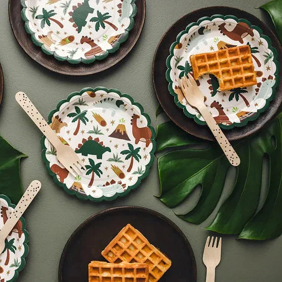 Ronde kartonnen dinobordjes met groene geschulpte rand en dinosaurusprint, op een gedekte tafel met wafels en bestek.