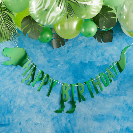 Groene dino-slinger met 'Happy Birthday' tegen een blauwe achtergrond, onder groene ballonnen en bladeren.