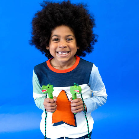 Kind houdt een dino-springtouw met groene dinosaurushandgrepen vast tegen een blauwe achtergrond.