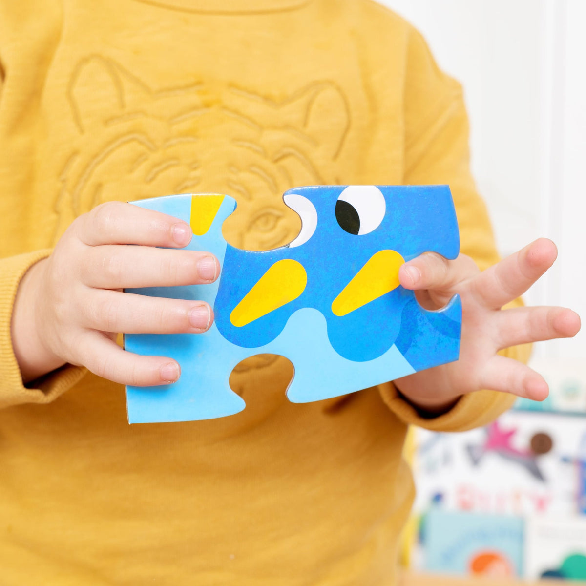 Kind in een gele trui houdt een groot blauw puzzelstuk van Tower Puzzel Dino vast.